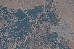 Aerial photo of the modern town of Firuzabad and the ancient circular city of Gor nearby. Greenery seen from above with segmentation due to infrastructure visible; a large circular segment is prominently featured.