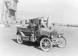 Photograph of a British armoured car with a driver and passenger outside Aleppo, with a white flag of truce set on it