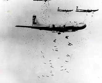 Black and white photo of three multi-engined aircraft flying in formation while dropping a large number of bombs