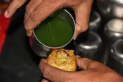 A green, watery sauce is poured into a filled panipuri