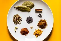 Various spices of different colours, whole or ground, arranged in small piles on a white plate.