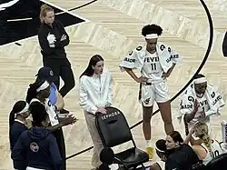Indiana Fever players and coaches gather in a huddle during a timeout at a WNBA game in Chase Center.