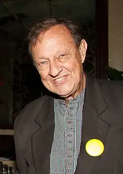 Tightly-cropped photo of smiling man in a striped collarless shirt and black blazer