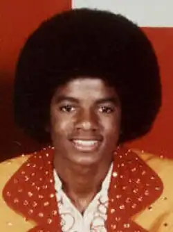 Jackson is wearing a yellow and red suit while sporting an afro for his haircut. His skin is dark