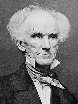 A daguerrotype of an elderly man with startling white curly hair standing out from both sides of his head.