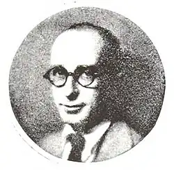 Man with thinning hair wearing round glasses, a suit, and a tie