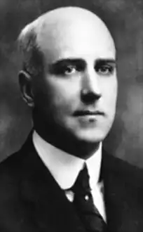 A black-and-white portrait of a man in a suit and tie, looking slightly to his right.
