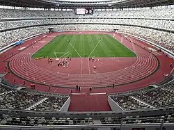 Photo of eleveted seats around a red athletics track and a green grass field.