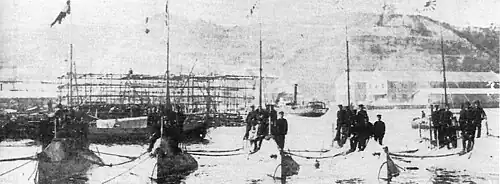 Five submarines moored next to each other with men standing on them