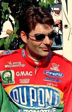 A man in his mid-twenties wearing sunglasses and rainbow-colored racing overalls