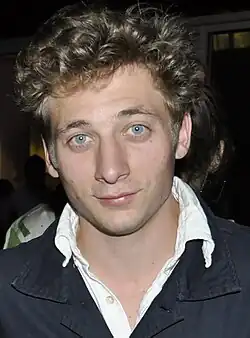 A white male with blond hair and light blue eyes smiles at the camera