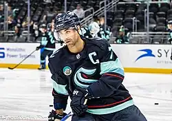 Ice hockey player holding a stick and wearing a helmet, featuring a letter C on the top right