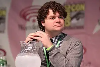 Morris speaking at the 2013 WonderCon at the Anaheim Convention Center in Anaheim, California. He is clean shaven, but has a very curly head of hair.