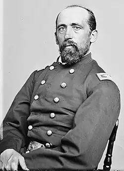 Black and white photo shows a balding, bearded man wearing a dark uniform with two rows of buttons.