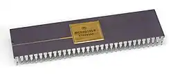 Close up of a small dark grey rectangular microprocessor chips with small gold-colored metallic prongs extending from the side downward. The top has a small gold plate in the middle that reads "MC68010L8, 1TA28552".