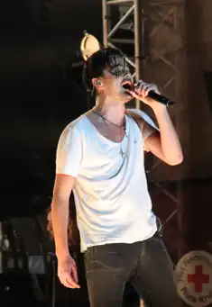 blurry image of Dinand Woesthoff wearing a white t-shirt and black jeans, singing into a microphone onstage with eyes closed