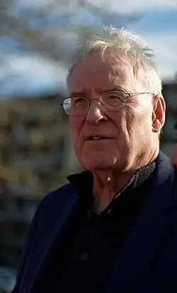 Middle-aged man wearing a dark blue suitcoat, black dress shirt, and silver-rimmed eyeglasses