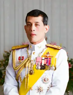 Portrait photograph of King Rama X in a white uniform decorated with medals on his left chest and yellow sash