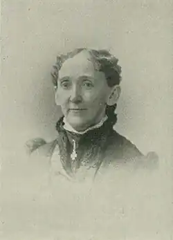 B&W portrait photo of a middle-aged woman wearing a dark, high-collared blouse with her hair in an up-do.