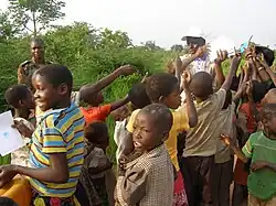 a group of children surround a man holding notebooks