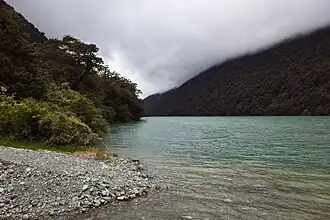 A blue-green lake in a forested valley covered by low cloud