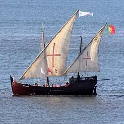 Modern replica of a lateen-rigged caravel under sail in Lisbon harbor.