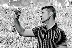 A black-and-white upper body photo of Binford inspecting a tool in his extended hand