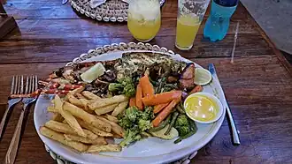 A plated cooked lobster served with chips, carrots, broccoli, and dipping sauce at a seaside lodge