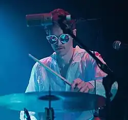 Louis Cole in 2018 within blue lighting playing drums.
