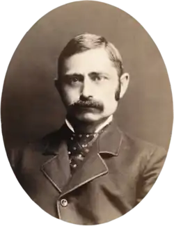Oval sepia image of a mustachioed man with sideburns in a suit with an ornate tie
