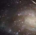 This Hubble image features a close-up view of the outer arms of the spiral galaxy NGC 45. These spiral arms are filled with tiny blue dots - stars - and glowing pink clouds - star-forming nebulae. This is shown against a dark background.