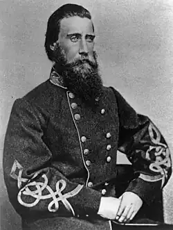 Black and white photo of a bearded man wearing a dark gray military uniform with frogging on the sleeves.