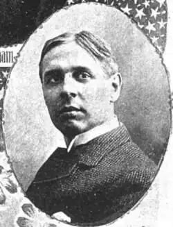 A man in his forties with thinning black hair wearing a black coat