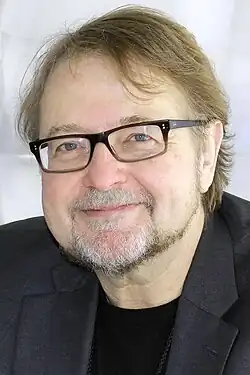 head and shoulders of Urrea with light brown hair, black glasses, with a goatee