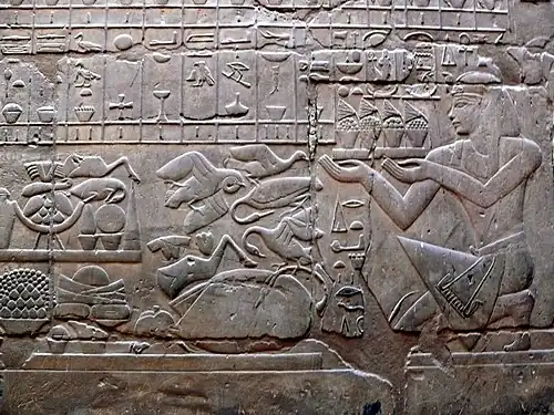 Relief of an ornately dressed man kneeling and holding a tray of food and flowers