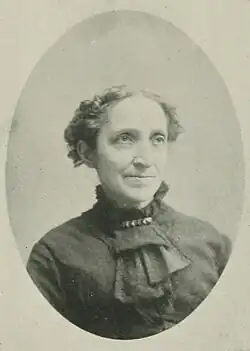 19th-century B&W portrait photo of a woman with her hair in an up-do, wearing a dark, fitted blouse.