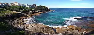 Mackenzies Bay, as a rocky inlet, in April 2013. The headland in the background is Mackenzies Point. Both are on the route of the Bondi to Coogee urban coastal walk,[21] which is visible in the upper-left.
