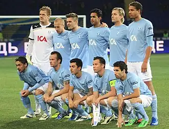 An association football team. A team of players in light blue shirts, white shorts and light blue socks, poses on a pitch for a formative shot.
