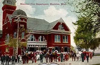 Colorized photograph of a fire station with horse-drawn equipment.