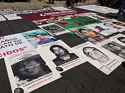 Posters spread on pavement outside; each poster has a photograph and name of a missing person