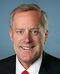 facial portrait of a smiling middle-aged man wearing a dark blue suit with a red tie