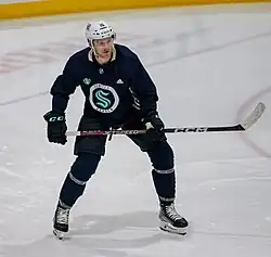 Ice hockey player in a Seattle Kraken jersey holding his stick up