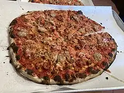 A pizza, topped with various meats, on a tray lined with parchment paper.