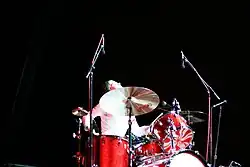 Meg White during a performance, sitting at a red drumkit glancing up to her left