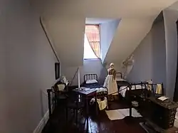 The servants' quarters in the attic. There are two sparsely-furnished beds. There is a window in the center, and the ceiling slopes down on either side.