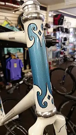 Close up of the steering head tube with off white paint highlighted by a metallic blue rectangle having scroll accents
