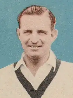 Portrait of Mervyn Roye Harvey, Australian cricketer, wearing a white cricket sweater with dark trim, smiling at the camera.