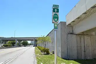 An asphalt path going into the background until passing under a bridge, with a sign in the foreground.