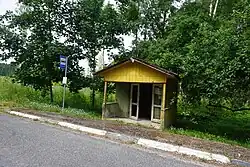 A little yellow bus stop amidst green trees