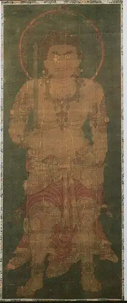 Frontal portrait of a frightening deity dressed only in a skirt-like garment holding a sword in his right hand.